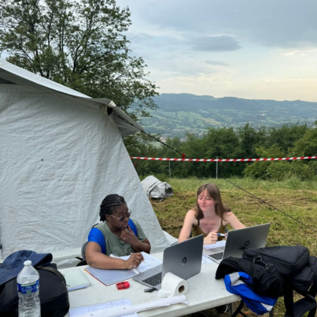 Deux élèves sur le terrain, elles sont assises à une table devant une tente.